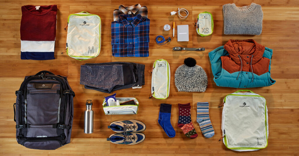  A variety of clothing, toiletries, and other items neatly arranged on a wooden floor, representing the essential items needed for a safe and comfortable journey during the Indonesian tradition of Mudik.